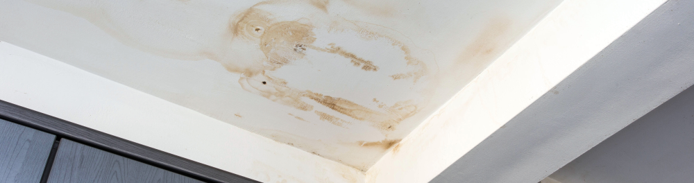 Ceiling corner with visible water damage and brown stains from a plumbing leak.