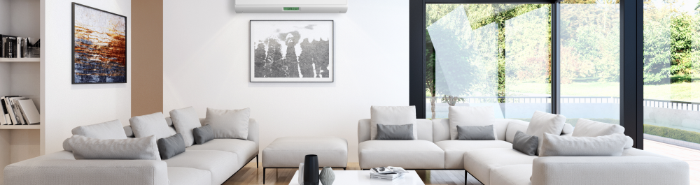 A modern living room featuring a sleek, wall-mounted air conditioning unit above a comfortable sectional sofa. Large floor-to-ceiling windows bring in natural light, highlighting the clean and minimalistic design of the space. This image emphasizes the integration of energy-efficient and eco-friendly air conditioning systems into contemporary home designs, aligning with sustainable living practices.