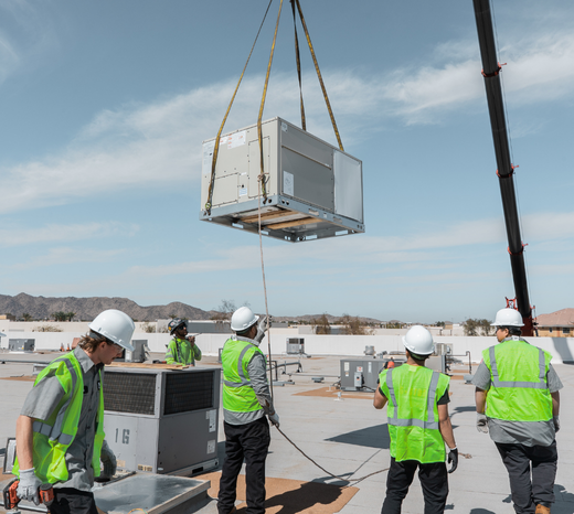 Rainforest's commercial AC install crew carefully watches as a new AC is lowered onto a roof from a crane.