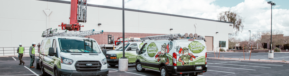 3 Rainforest Plumbing & Air vans sit outside a commercial building ready to start their day.